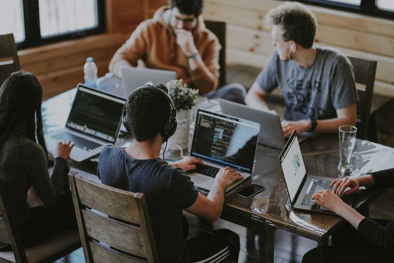 People working together at a long wooden table, each with a laptop and notes in front of them